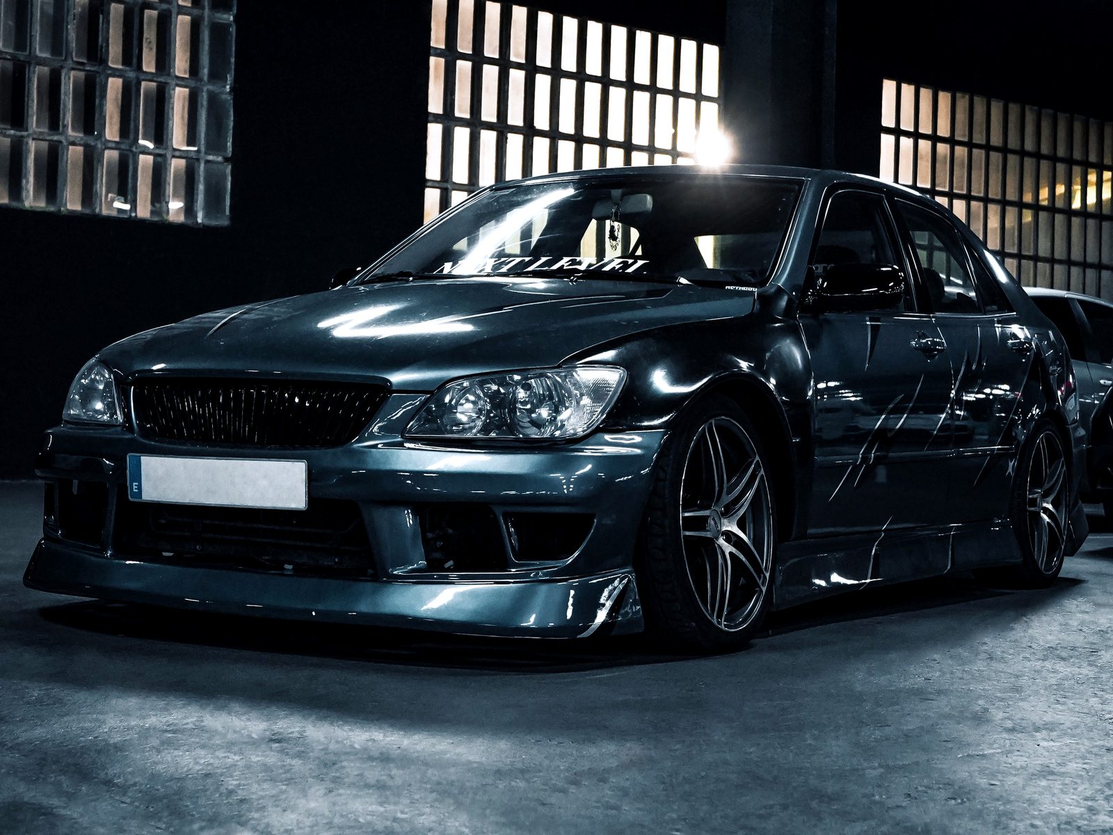 Modified Lexus IS sedan on aftermarket wheels in a dark garage