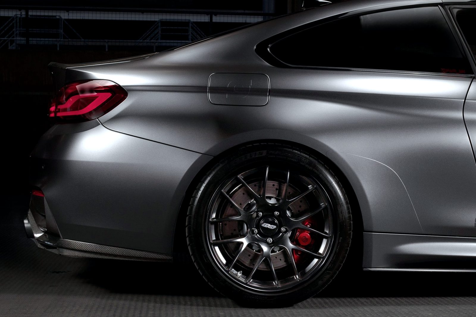 Gray BMW M4 rear quarter on a multi-spoke aftermarket wheel, studio lighting